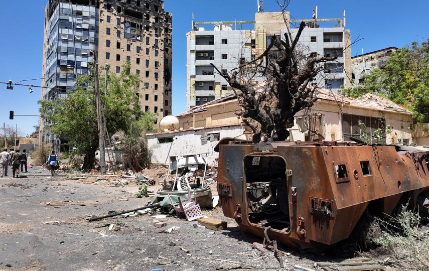 Members of the Sudanese army walk near a destroyed military vehicle and bombed buildings, as they retake ground in Khartoum from the paramilitary Rapid Support Forces, on 26 March 2025.