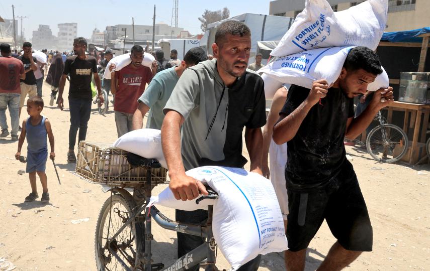 Palestinians carry sacks of flour as they gather to receive aid supplies in Khan Younis, in the southern Gaza Strip, June 26, 2025.