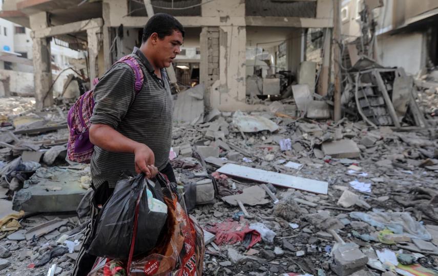A man is pictured walking through rubble and carrying items as Palestinians in Gaza City preparing to flee to the south as Israel threatens invasion.