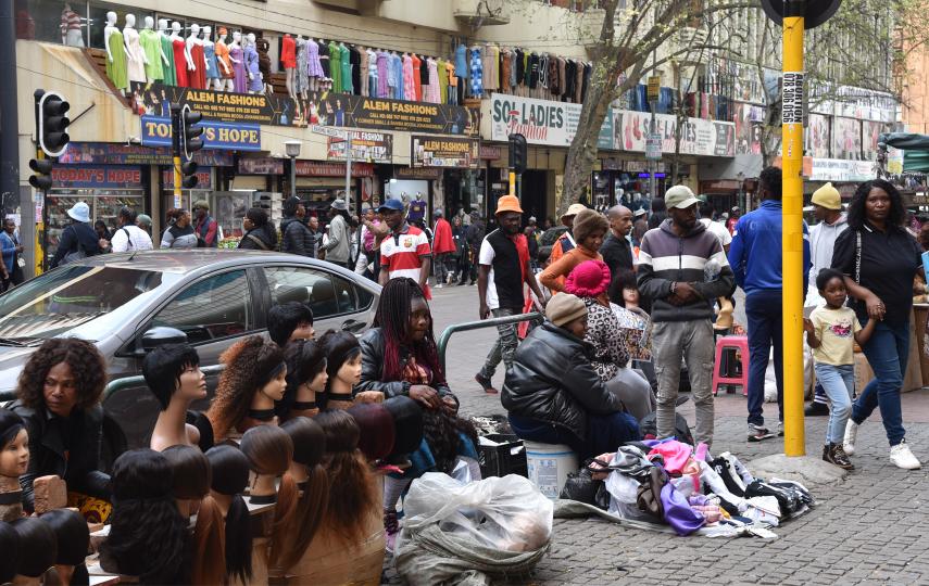 A picture of Rahima Moosa Street, still commonly known as Jeppe, there are people walking, clothing shops in the background, and head mannequins with wigs in the foreground.