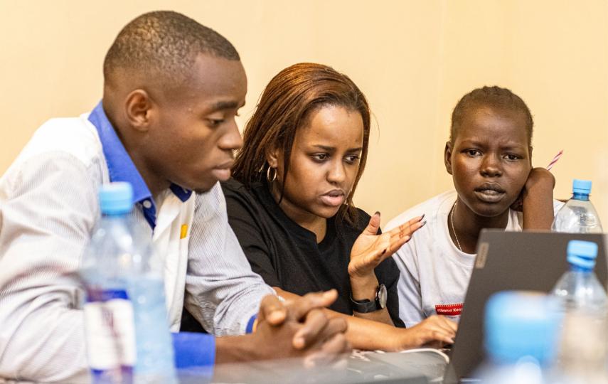 Three people sit and discuss in front of a computer during a training on resource mobilisation in Kakuma camp by the refugee-led organisation, Solidarity Initiative for Refugees.