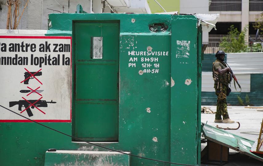 A Kenyan police officer, a member of the Multinational Security Support (MSS) mission in Haiti, guards the remains of the General Hospital in Port-au-Prince, in July 2024. The sign reads: “Do not enter the hospital with a weapon.”