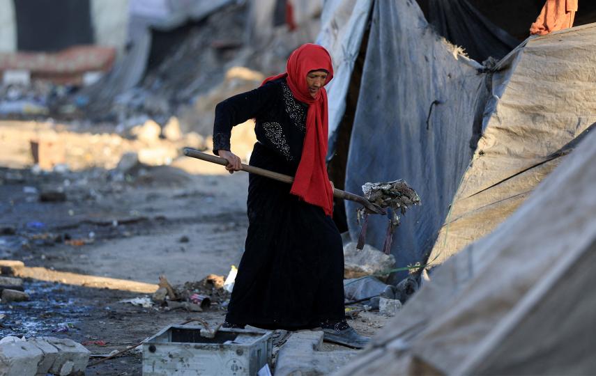 A Palestinian woman cleans an area next to tents, amid a ceasefire between Israel and Hamas, in Gaza City, October 14, 2025. 