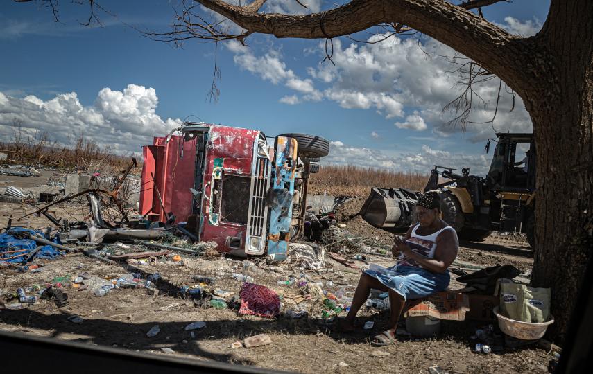 Amidst scrap metal and garbage, a woman rests in the shade while heavy machinery removes debris in the town of Black River. 