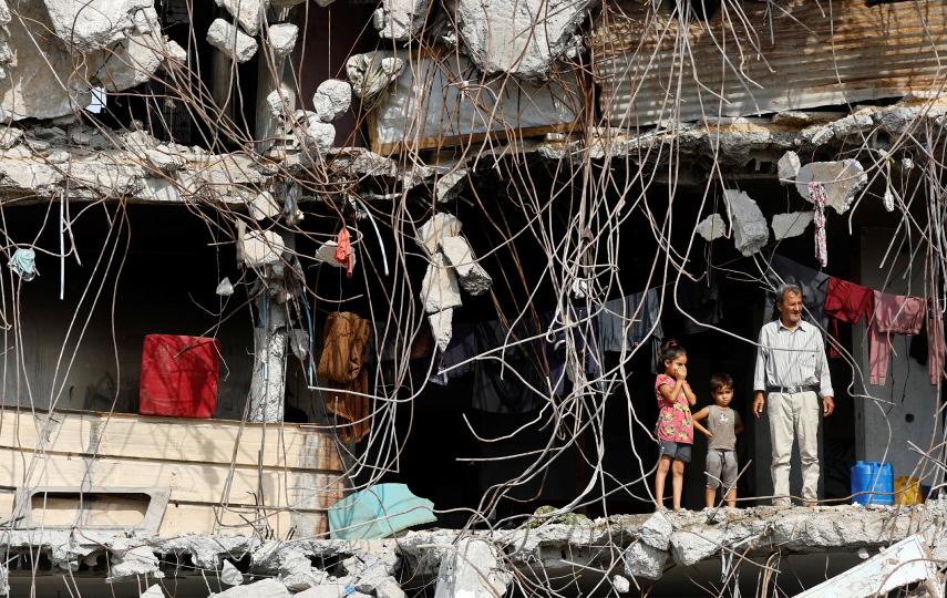 A Palestinian man and children stand at a heavily damaged building surrounded by rebar and rubble, amid a ceasefire between Israel and Hamas, in Gaza City, November 2, 2025. 