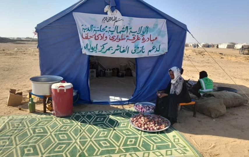 A large blue tent with a sign on the front in an arid landscape, a mat lays outside of the tent door