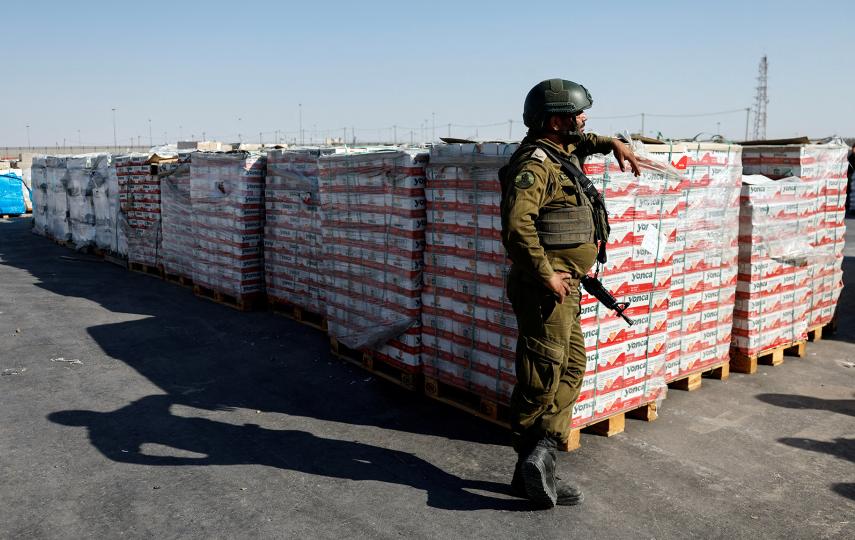 An Israeli soldier stands next to the parcels of humanitarian aid awaiting to be transferred into Gaza from Israel, at the Gaza part of the Kerem Shalom crossing in the Gaza Strip, July 24, 2025.