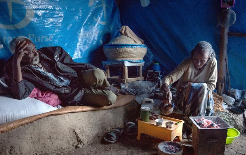 An elderly woman serves coffee as an old man leans back on a seat and looks out of the tent he lives in at the 70 Kare IDP Center refugee camp in the town of Mekele, capital of Tigray.