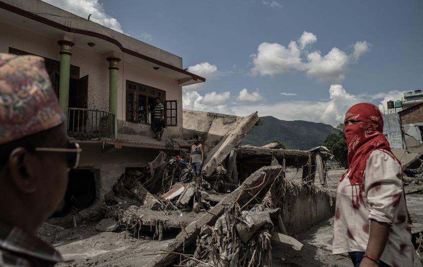 Two people in the foreground with buildings and destruction behind.