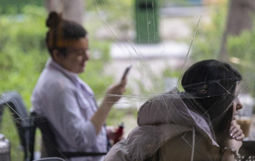 Image of cracked glass with two people, one on their phone, in the background.