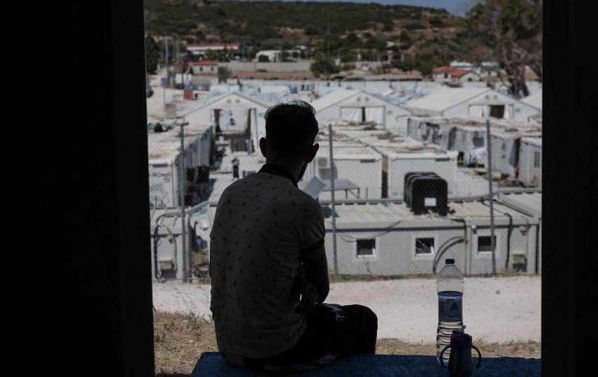 A photo of a the shadow of a refugee as he looks at the temporary Kara Tepe Refugee Camp on the Greek island of Lesvos in June 2025.