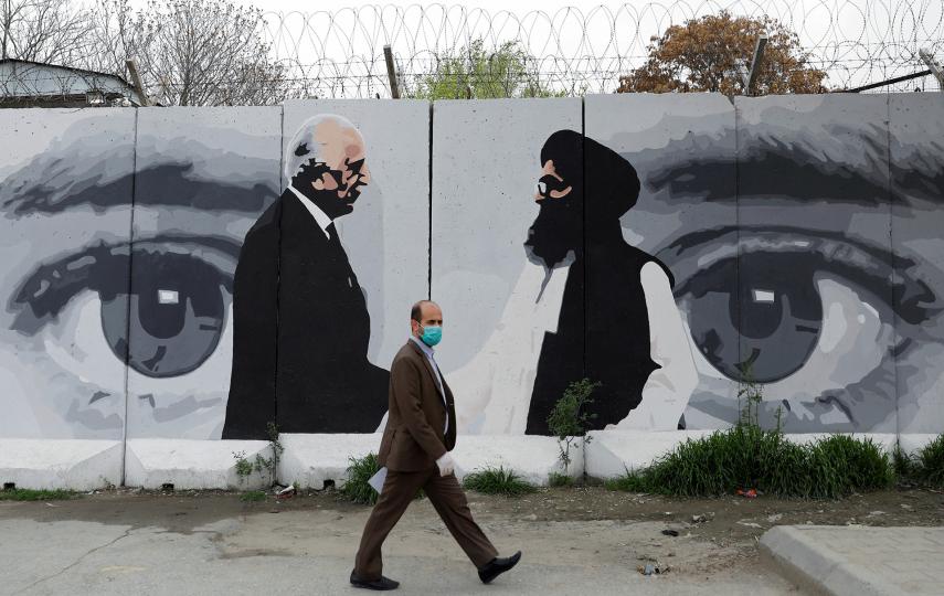 An Afghan man wearing a protective face mask walks past a wall in Kabul