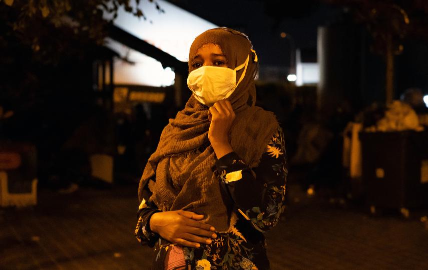 A woman stands in the dark, her face illuminated by faint street lights.