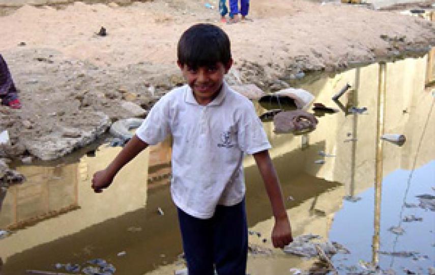 [Iraq] Young boy stands on the edge of sewage outflow.