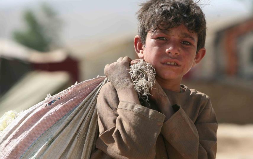 A young boy carries a heavy bag in an IDP camp in Kabul, Afghanistan June 2008. The upsurge of fighting in southern Afghanistan during 2006 has compelled tens of thousands of people to flee their homes to seek temporary refuge with relatives and friends i