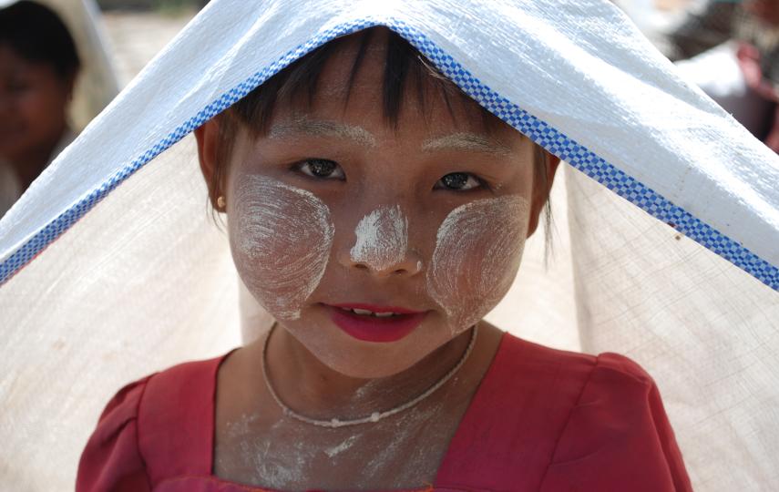 Eight year old Sanhla lost her mother when Cyclone Nargis struck nearly one year ago. She shields herself from the sun using a rice bag while patiently waiting with her grandmother to collect various food items being distributed. The communities hit by Na