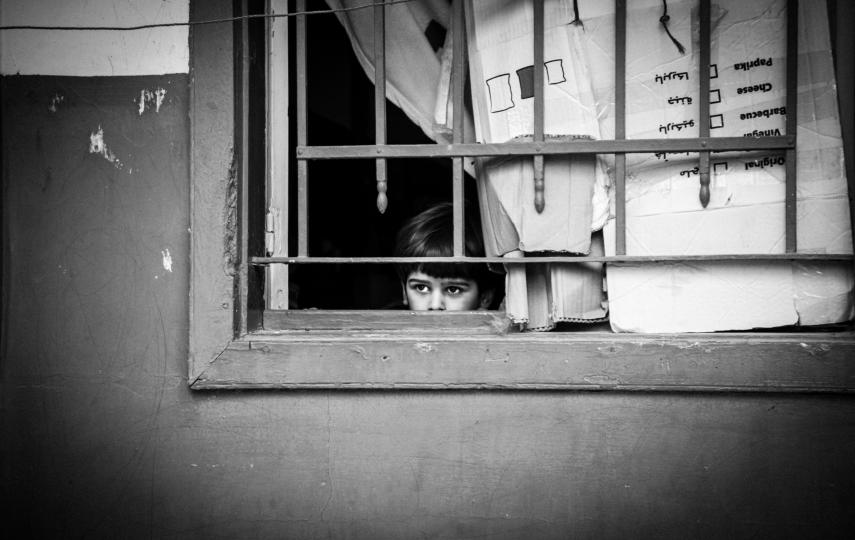 A young Syrian refugee child in al Marj village in Lebanon's Beka'a Valley peers out of his makeshift window, where cardboard protects from the sun's heat