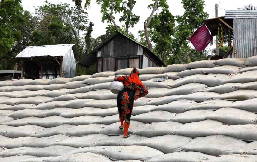 Photo of a woman in Bangladesh walking up a mountain of sand bags from the river