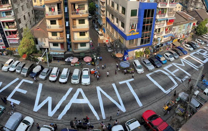 An aerial view of a urban street in Yangon, Myanmar where the words "We want democracy" have been painted large onto the street surface.