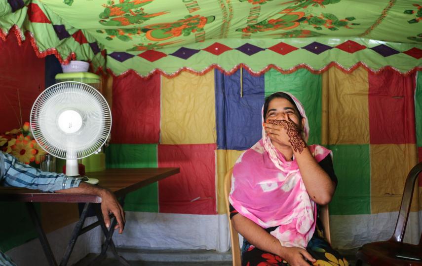 Photo of Romida Begum sitting inside with her hand covering her smiling mouth