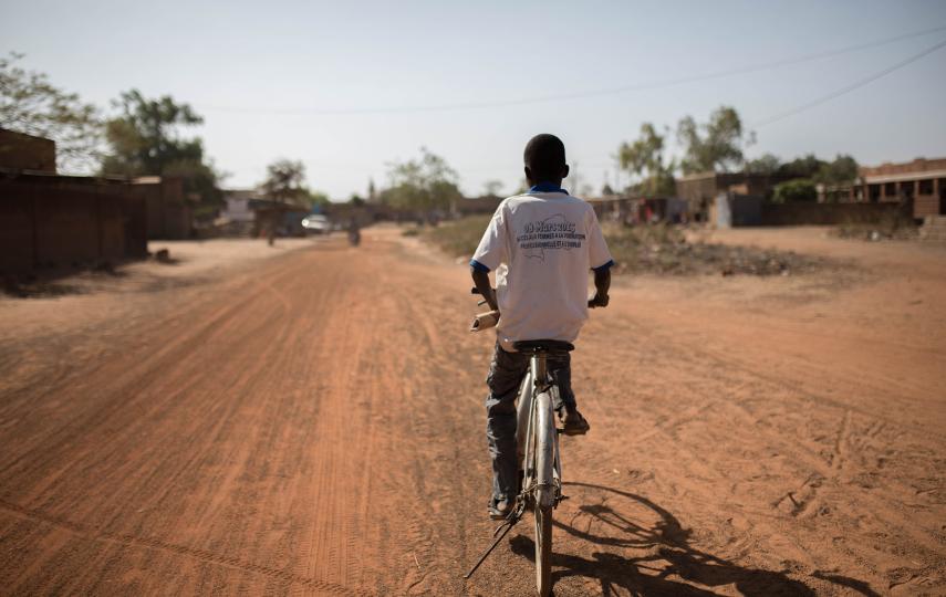 A young person rides on a bike on a dirt road away from camera