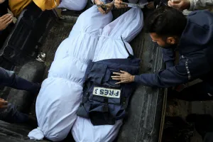 A photo of mourners as they gather around the bodies of two Palestinian journalists who were killed in Israeli strikes, amid the Israel-Hamas conflict. Their bodies are wrapped in white sheets and one has a press vest on it.