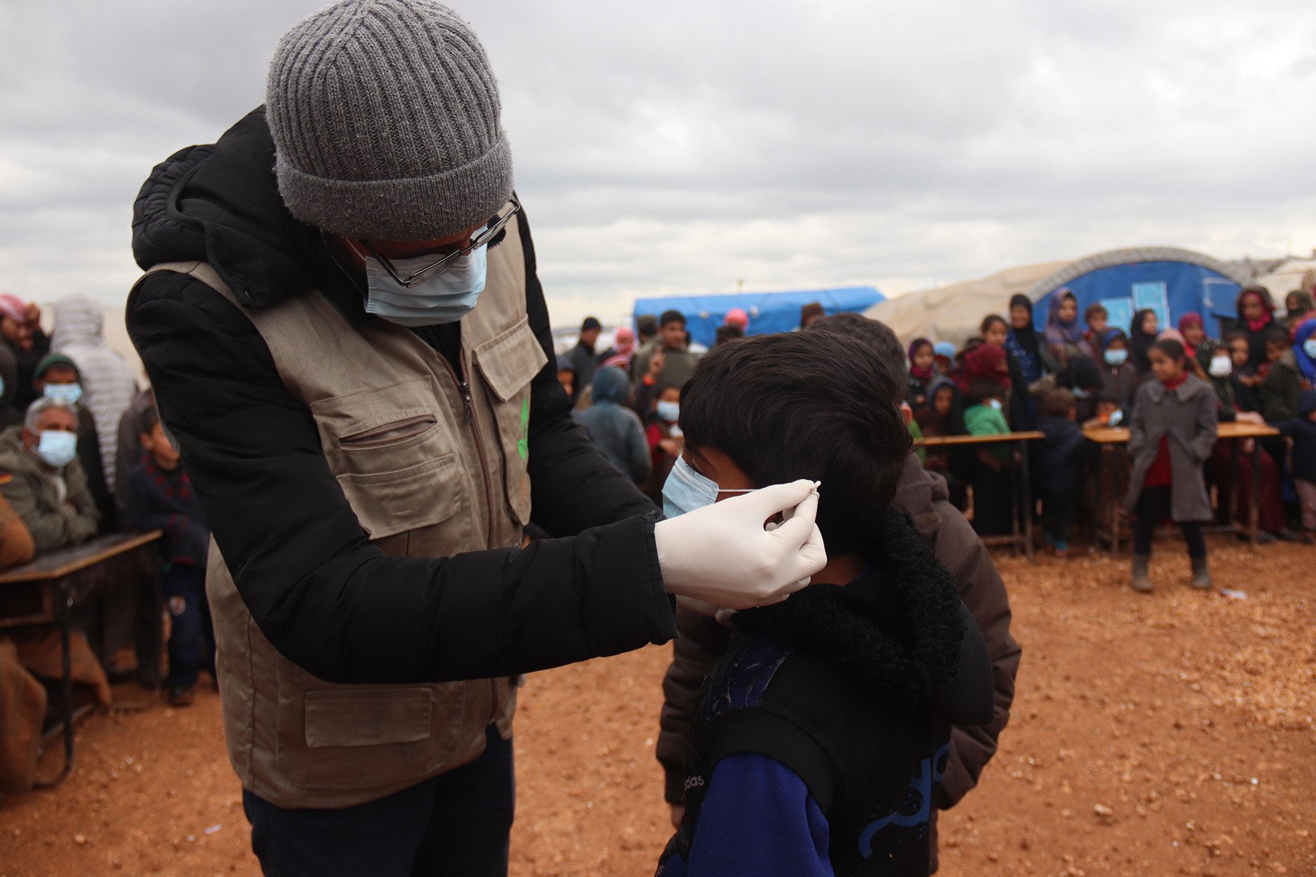 An aid worker shows a child how to put on a protective mask