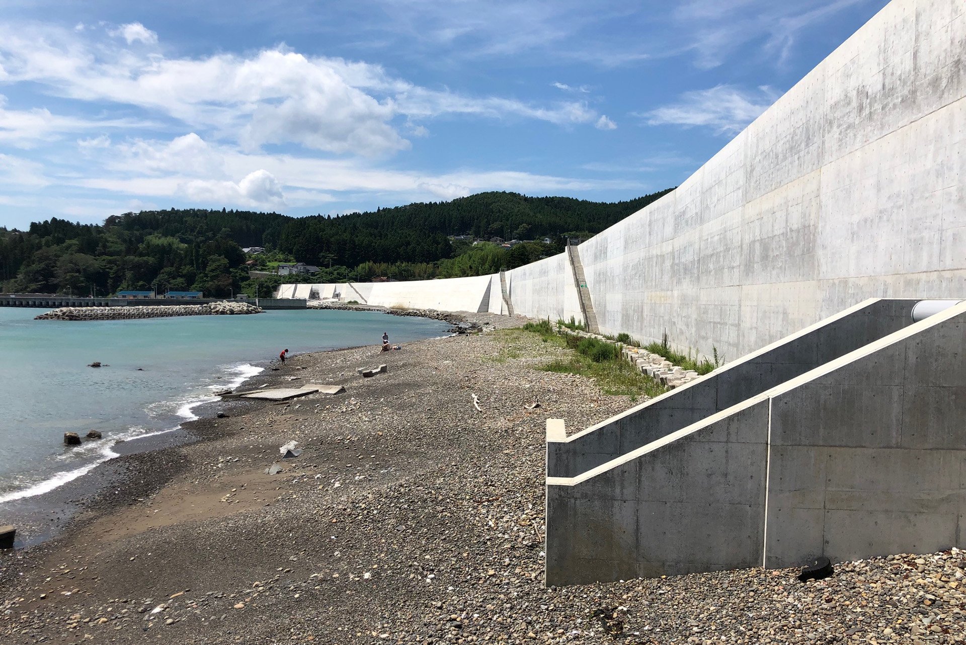 A large cement wall runs along the length of a beach-shoreline.