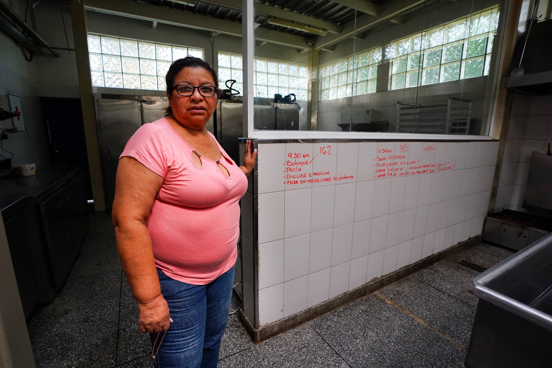 A woman stands in a commercial sized kitchen area with notes written directly on the wall