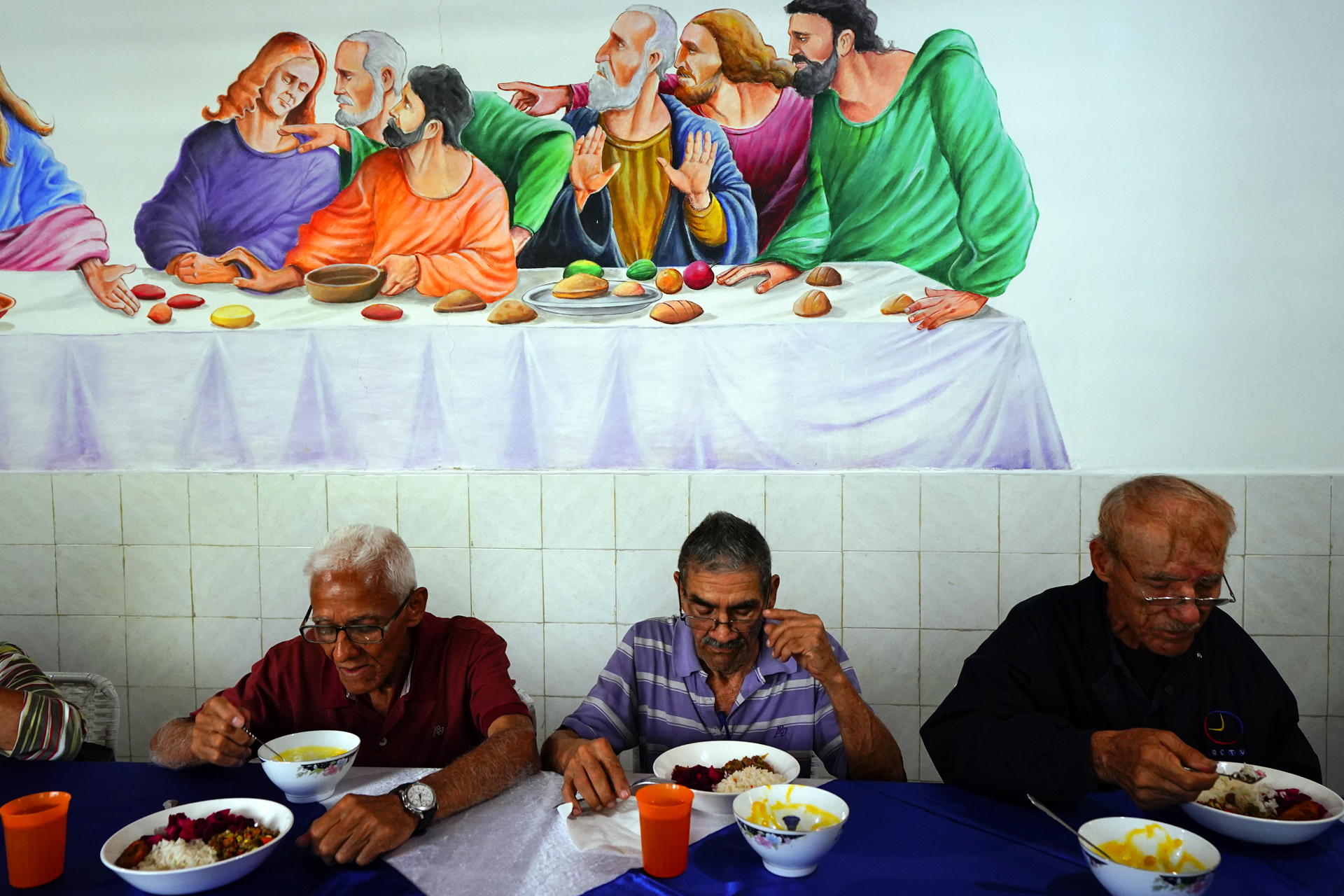 Elderly people sit eating in front of a mural of the last supper in similar positions accidentally