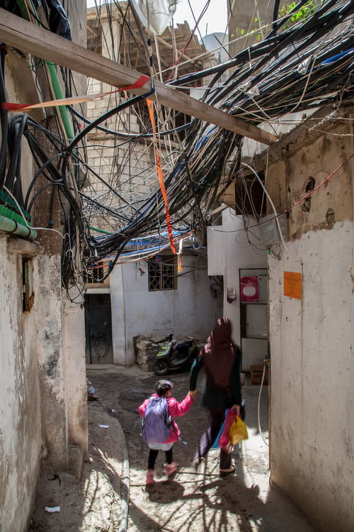 A woman and a child walk underneath many disorganized and loose wires.